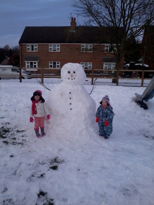 Izzy and Macey standing next to the big snowman that they built in Markington! by Becci Paul