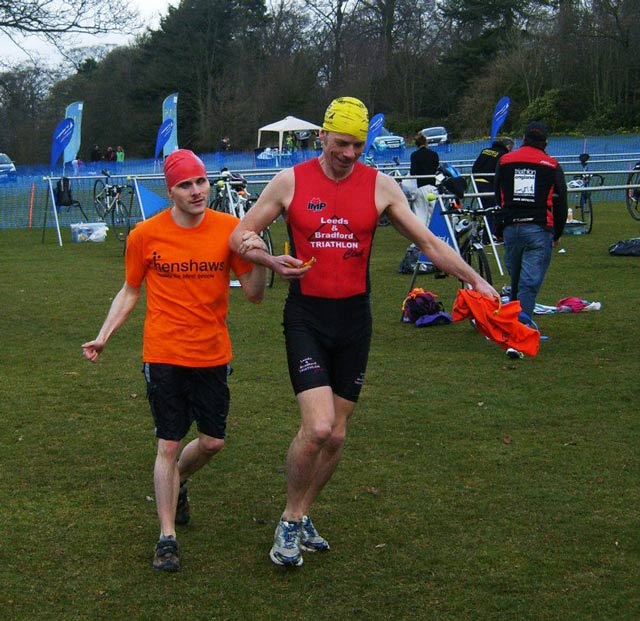 Michael running to the transition area after completing his swim, supported by Matt Michael running to the transition area after completing his swim, supported by Matt
