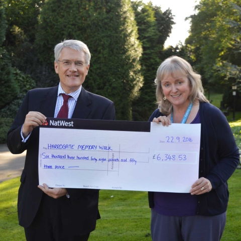 Andrew Jones MP hands a cheque for £6,348.53 to Alzheimer’s Society Services Manager, Alison Wrigglesworth at the entrance to the Valley Gardens where the walk took place