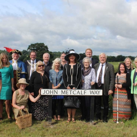 John Metcalf Way sign unveiling 2: Councillor Anne Jones, Mayor of the Borough of Harrogate; Councillor David Goode, Mayor of Knaresborough; Roger Hewitt, the Town Crier of Knaresborough;  local historian Brian Forshaw; Bernard Higgins and other representatives from the Blind Jack of Knaresborough Tri-centennial Anniversary Committee, the FEVA Knaresborough committee and Welcome to Yorkshire celebrate the unveiling of  the road sign in honour of John Metcalf
