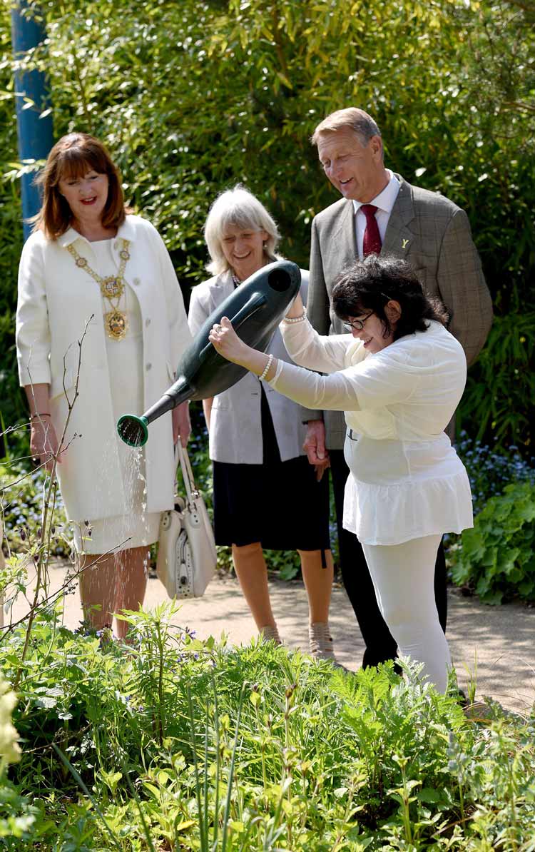 Art Maker Hannah Reda waters the plants at the Arts & Crafts Centre watched by Anne Jones, Barry Dodd, and Frances Dodd