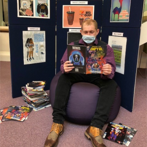 Library assistant Tom Bamford, sitting in front of the exhibition at Harrogate library, samples one of the comics in the giveaway