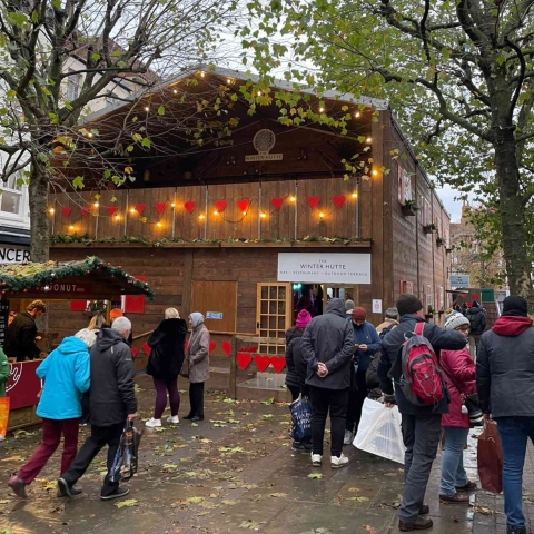 SWISS CHALET POP-UP BAR & RESTAURANT OPENS AT YORK CHRISTMAS MARKET TO FANFARE FROM ALPINE HORN AND CAPACITY VISITORS [21 NOVEMBER 2022, YORK]: York’s newest Christmas attraction opened on Friday to a fanfare with a difference – from a traditional alpine horn. The Winter Hütte Swiss-style bar and restaurant brings a true taste of the Alps to York’s Christmas Market and during its opening weekend entertained thousands of residents and tourists who came to enjoy the new ski lodge ambience, with capacity visitors in the bar and over 800 people served in the upstairs restaurant. The two-storey Winter Hütte is a traditional wooden chalet built around a marquee structure, complete with mountain views, red shutters, window boxes, and even rustic cow bells. The pop-up venue comprises a fully-licensed bar area downstairs serving seasonal favourites such as gluhwein and hot chocolate, as well as a special Alpine Star beer from Brew York and a range of cocktails and wines. A gourmet sausage stall The Dog Haus caters for bar patrons as well as passers-by outside. With its Alpine folk motif curtains, vintage ski posters and sheepskin-covered wooden stools, The Winter Hütte’s apres-ski bar evokes a cosy mountain refuge, with a large stone fireplace and woodburning stove, and window views of snowy village scenes. With live music performances and the scent of gluhwein and bratwurst, The Winter Hütte offers an experience for all the senses this Christmas. Upstairs The Star Inn at The Winter Hütte brings a relaxed bistro-style restaurant and Swiss-with-a-twist food from one of Yorkshire’s Best-known chefs, the Michelin-starred Andrew Pern, while the outdoor terrace makes a picturesque setting for a festive drink overlooking the Christmas Market. With a broad menu including traditional favourites such as fondue and tartiflette as well as off-piste specials such as pheasant with smoked garlic and a ‘Mont Blanc’ dessert, the ambience is completed by antler chandeliers and stunning black and white vintage photographs from the Swiss village of Zermatt, creating an authentic and cosy dining experience, with table-sharing in true apres-ski style. Booking is recommended for the restaurant as well as the outdoor drinks terrace at www.winterhutte.co.uk. A deposit of £15 per person is required for the booking and will be fully redeemable against the final bill. For full terms and conditions, please visit the website. The Winter Hütte is open every day from 17th November 2022 until 1st January 2023, from 9.30am until 11pm (closed on Christmas Day). For any general enquiries, please visit the website or email the team at CanIAlpYou@winterhutte.co.uk. The Winter Hütte is part of St Nicholas Fair, York’s Christmas Market, in collaboration with Make It York. The Winter Hütte is a joint venture between Coopers Marquees, CMJ Events and The Star Inn the City (York). Combined, the team brings over 60 years of live entertainment and food knowledge to deliver this spectacular new event for York, home to all three companies.