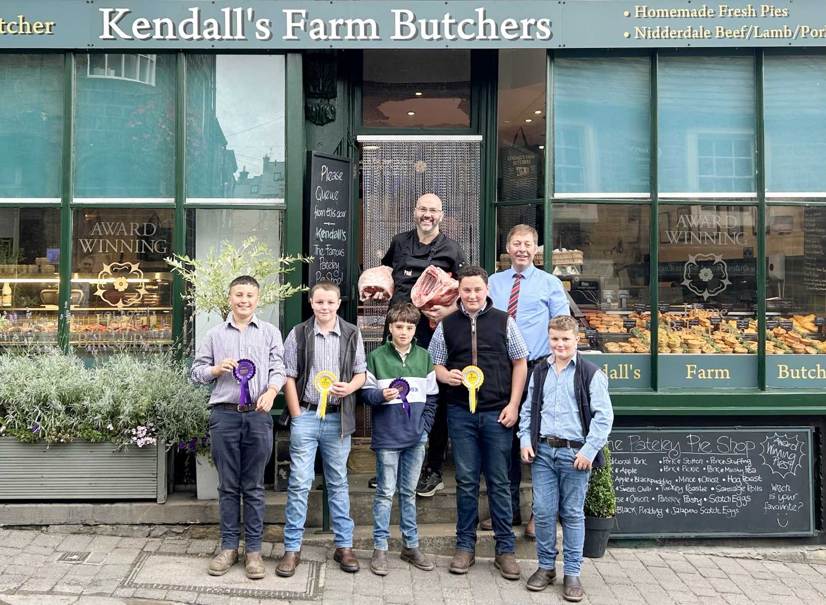 Young farmers with their rosettes at Kendall’s Farm Butchers in Pateley Bridge. From left are John Peel, Archie Hotham, Freddie Barrett and Thomas Marshall, with Archie’s brother Duncan also getting in on the act. Holding some of the prime lamb cuts is owner Paul Kendall, the group completed by Skipton Auction Mart’s livestock sales manager and auctioneer Ted Ogden
